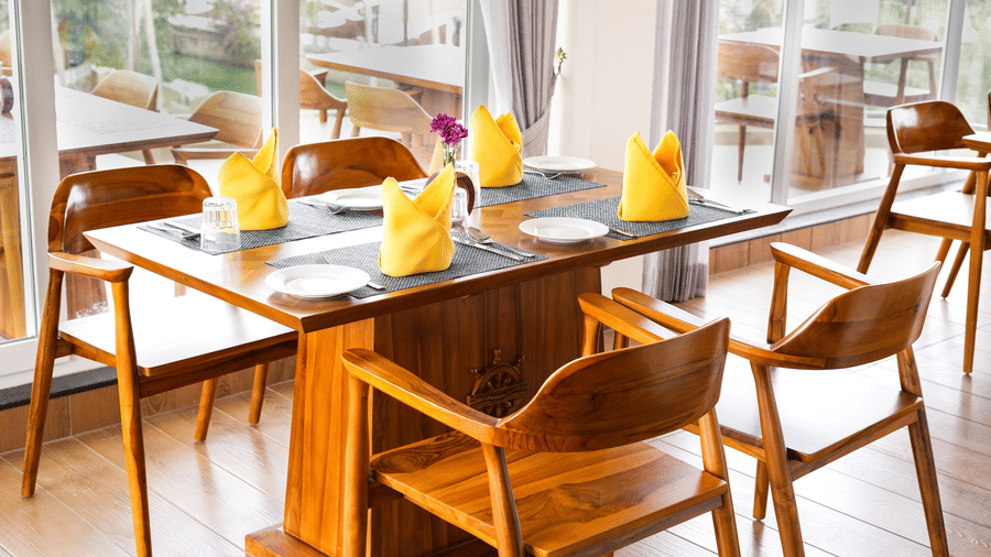 A dining table set with yellow napkins, silverware, and glassware, overlooking a lush green landscape - MGM Beach Resorts.