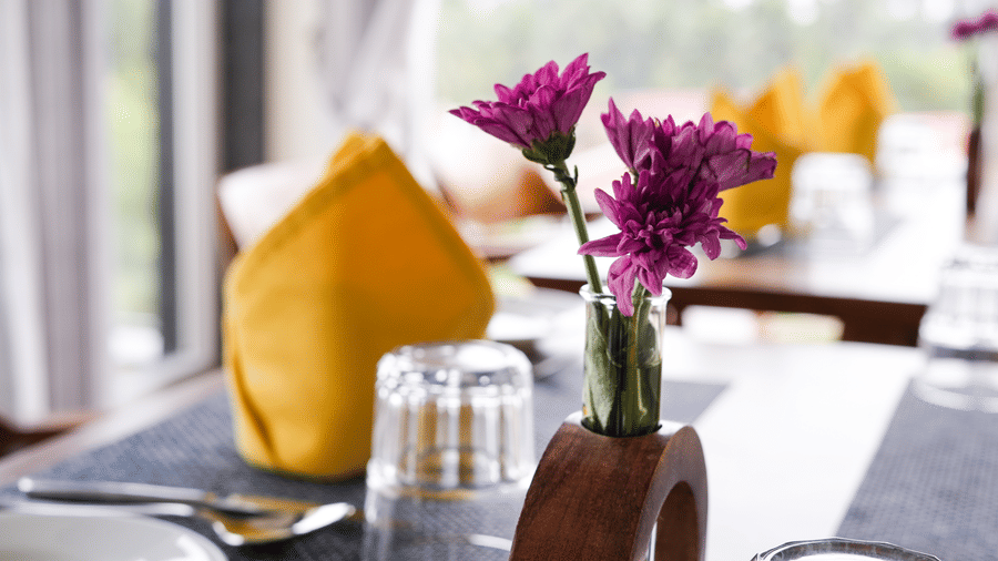 A close-up of a table setting with a vase of purple flowers, a yellow napkin, and silverware - MGM Beach Resorts.