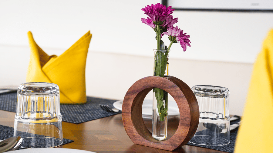 A close-up of a table setting with a vase of purple flowers, a yellow napkin, and silverware - MGM Beach Resorts.