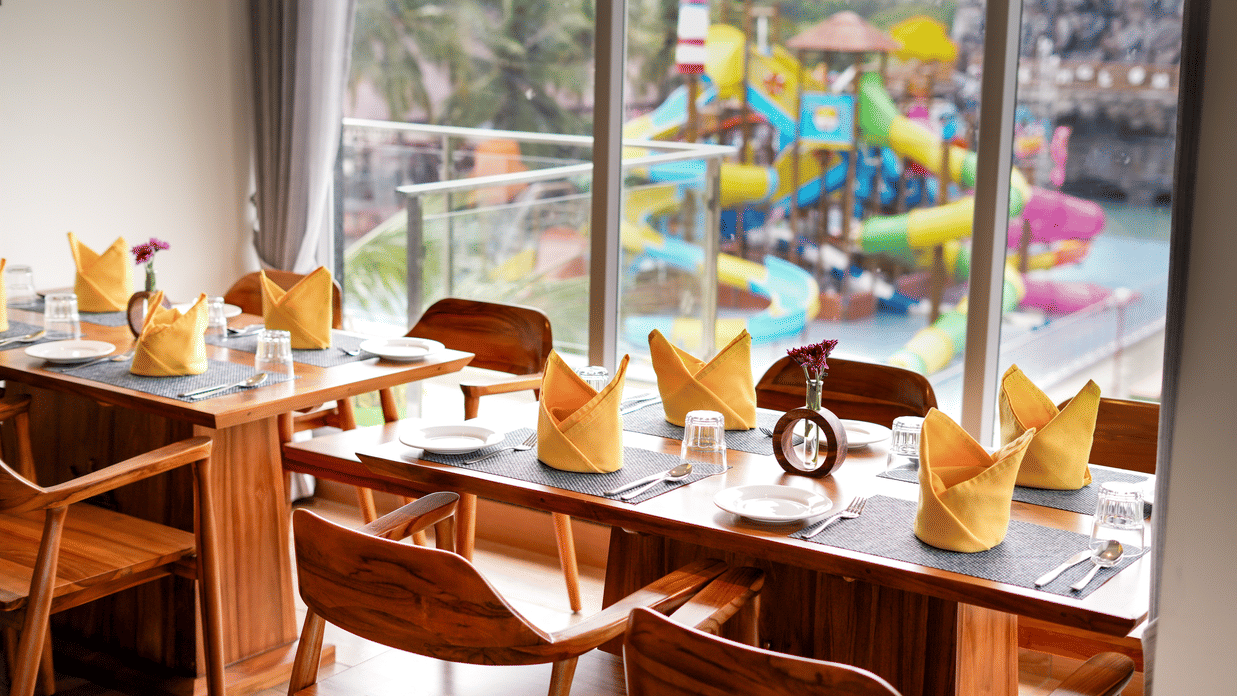 A dining area with wooden tables and chairs, overlooking a vibrant water park - MGM Beach Resorts.