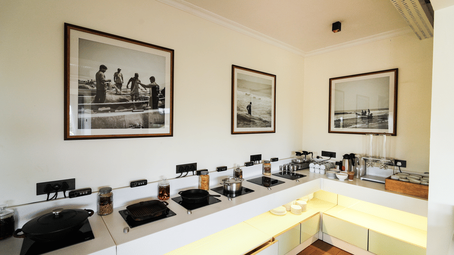 A modern kitchen area with a breakfast buffet setup, featuring framed black and white photographs of people surfing on the wall - MGM Beach Resorts.