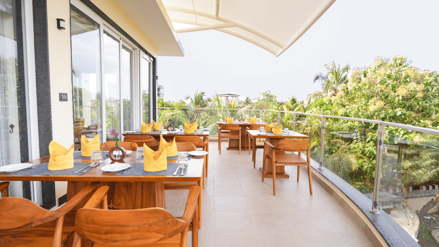 A spacious outdoor dining area with wooden tables and chairs, overlooking a lush green landscape - MGM Beach Resorts.