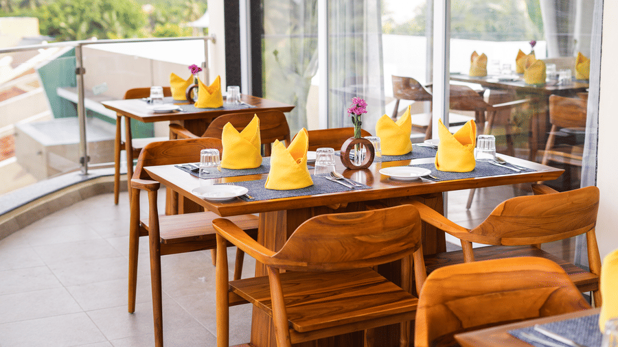 Wooden tables and chairs set up on a balcony, overlooking a green landscape - MGM Beach Resorts.