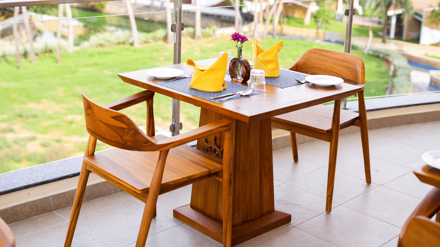 A romantic table setting for two on a balcony overlooking a lush green landscape and a pool - MGM Beach Resorts.